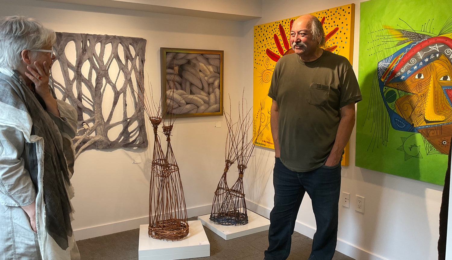 Mi'kmaq Artist Alan Syliboy standing in front of two of his paintings at The Prow Gallery in Halifax.