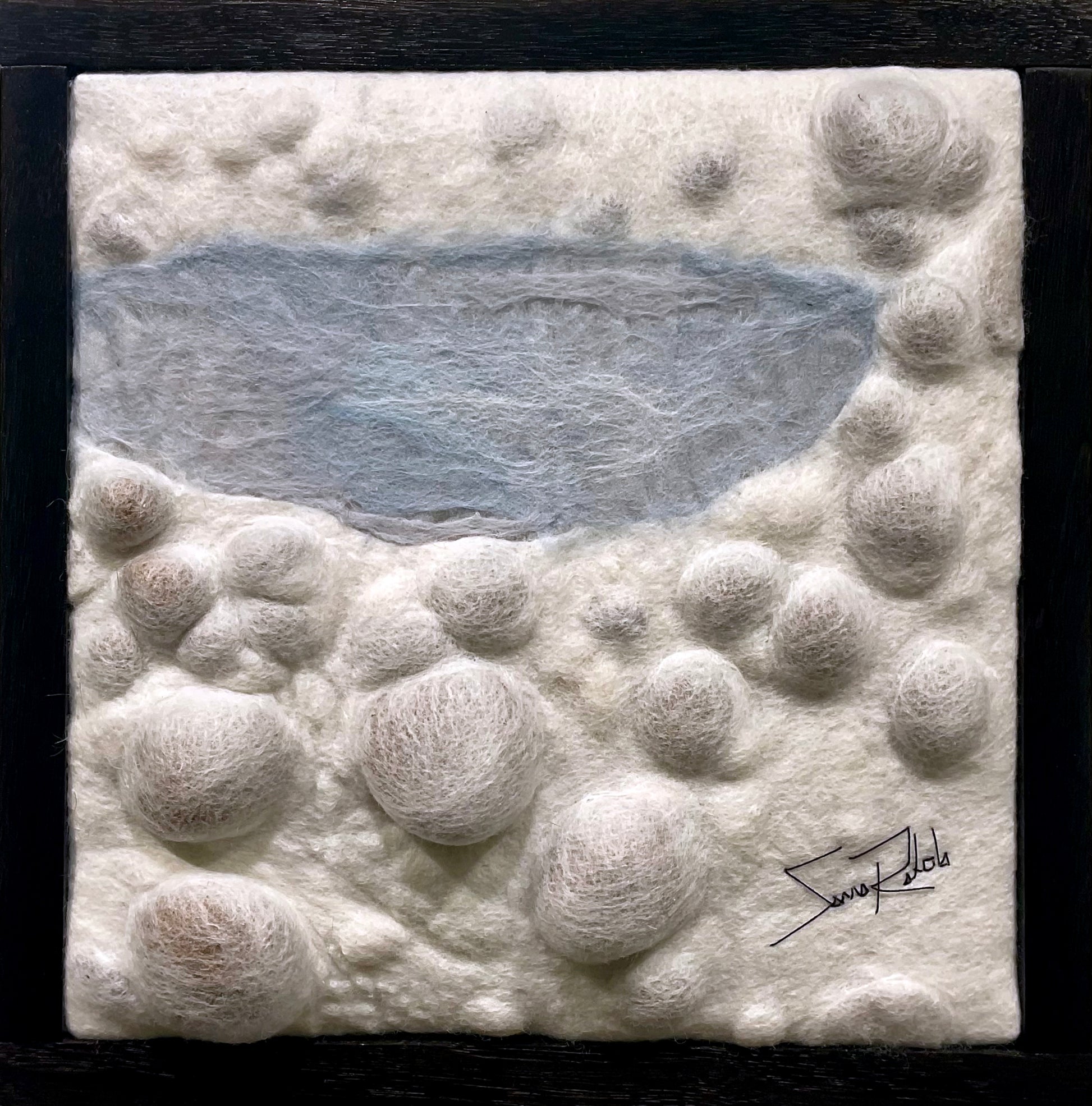 Textured white surface with circular patterns and a black signature in the corner, framed in black.